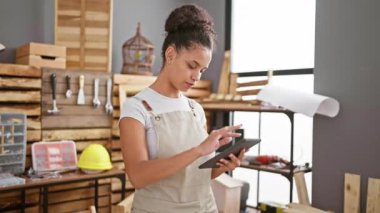 Marangozlukta ustalaşan parlak, genç İspanyol bir kadın, işinde çok iyi, ahşap işçiliğinin ortasında dokunmatik ped kullanıyor.