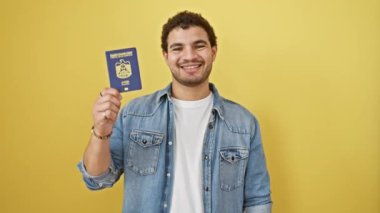 Neşeli genç Arap adam, kendine güveni tam bir pasaport taşıyor, neşeli bir işaret veriyor, sarı arka planda, pozitif başarı titreşimleri yayıyor.