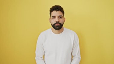 Modaya uygun sakallı neşeli bir genç adam, Latin-Arap titreşimleri, büyük bir gülümsemeyle sana bakıyor, iyi enerji saçıyor. Yakışıklı ve neşeli. Soğuk sarı bir duvarda izole edilmiş..