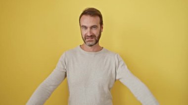 Mutlu, orta yaşlı, sakallı İspanyol bir adam, izole edilmiş sarı arka plana karşı duruyor, güvenle işaret ediyor, parmaklarıyla altı numarayı gösteriyor, mutlu bir gülümseme yayıyor.