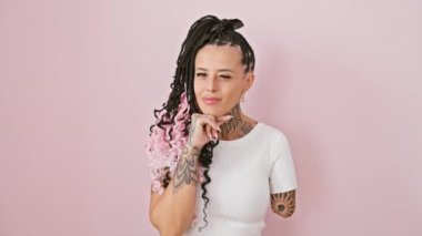 Düşünceli bir İspanyol ampüte kadın ayakta, elleri çenesinde, soru üzerine düşünüyor düşünceli bir gülümsemeyle - pembe arka planda izole edilmiş