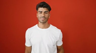 Beyaz tişörtlü yakışıklı genç adam canlı kırmızı bir duvara karşı pozitif bir tutum sergiliyor..