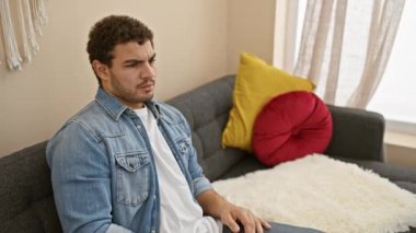 Apartmanındaki koltukta oturan şoke olmuş Arap adam, yüzle yüzünü kapatıyor, utangaç ve ürkek bir ifadeyle parmaklarının arasından bakıyor..