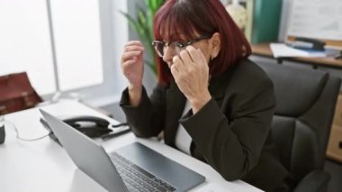 Düşünceli İspanyol bir son sınıf öğrencisi ofis masasında oturup dizüstü bilgisayar üzerinde çalışırken düşünüyor..