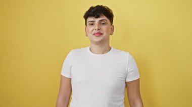Havalı, kendine güvenen, beyaz tişörtlü genç bir adam, sarı bir arka planda duruyor, neşe ve olumlulukla ışıldıyor. Başparmağıyla mükemmel bir onay işareti veriyor..