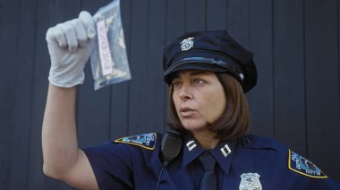 Üniformalı bir kadın polis elinde kanıt torbasıyla şehir zeminine karşı para tutuyor..