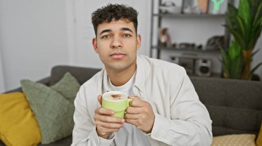 Yakışıklı bir genç, rahat, modern bir oturma odasında kahve içmekten zevk alıyor..