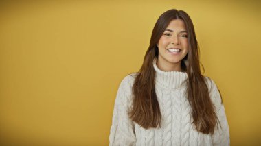 Beyaz kazaklı, gülümseyen, genç bir İspanyol kadın canlı, sarı bir arka plana karşı poz veriyor..