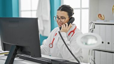 Genç, güzel İspanyol kadın doktor klinikte telefonla konuşuyor.