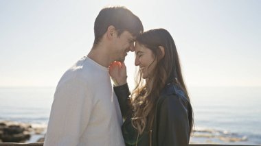 Gülümseyen bir çiftin, güneşli bir sahil kenarında burunlarını okşarken, arka planda okyanusla sevgi ve arkadaşlık sergilerken.