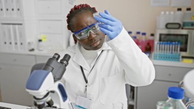Örgü ören Afrikalı Amerikalı kadın bilim adamı laboratuarda bir örnek inceliyor.