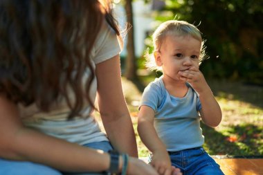 Anne ve oğlu bankta oturup parkta küçük solucanlar yiyorlar.