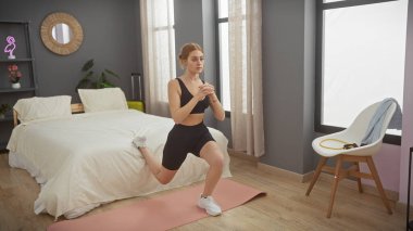 Genç bir kadın modern bir yatak odasında egzersiz yapıyor, spor yapıyor ve ev hayatı yaşıyor..