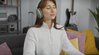 Rahat genç bir kadın, rahat bir oturma odasında kulaklıklarla müzik dinlemekten hoşlanır..