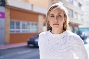 Sokakta ciddi bir ifadeyle duran genç sarışın kadın.