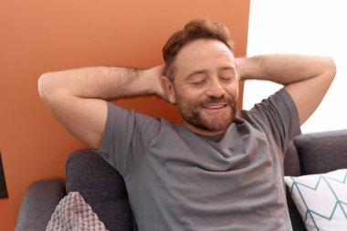 Middle age man relaxed with hands on head sitting on sofa at home