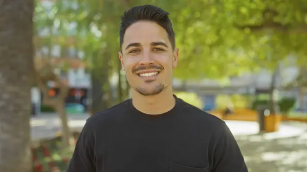 stock image Handsome young hispanic man smiling outdoors in a sunny green park.