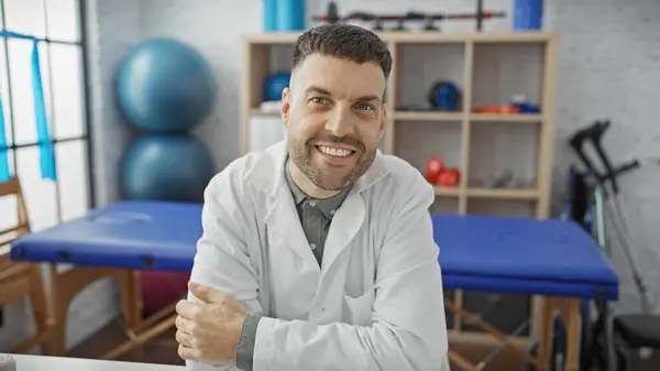 stock image Handsome hispanic man with a beard smiling in a physiotherapy clinic room.