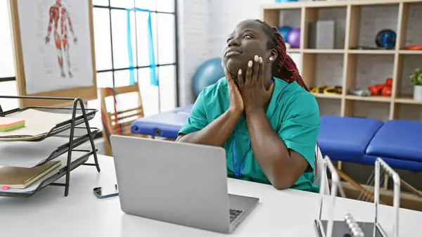 一位头戴辫子 体贴入微的非洲裔美国妇女躺在理疗诊所的办公桌前 在经过一番思考后 终于明白了 — 图库照片