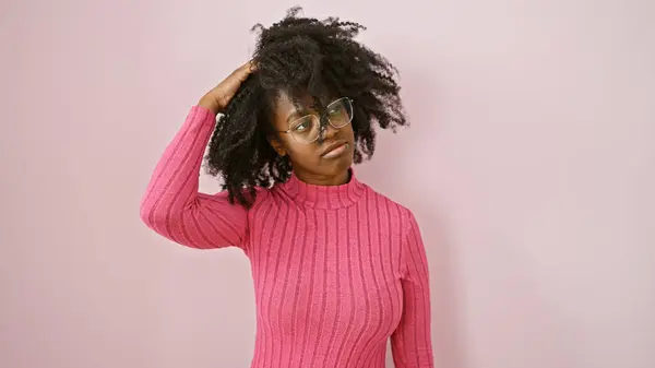 Stock image A contemplative african american woman in glasses posing indoors against a pink background.