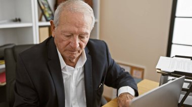 Odaklanmış, olgun bir iş adamının portresi. Ofis masasında oturuyor. Dizüstü bilgisayarına dalmış. Bu yaşlı, zarif patron profesyonellik sergiliyor..