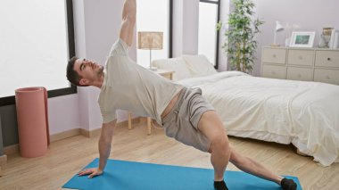 Genç bir adam, parlak bir yatak odasında egzersiz yaparken, sağlıklı bir yaşam tarzını yansıtıyor..