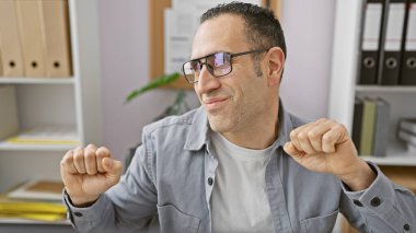 Modern bir ofiste gözlüklü, gülümseyen bir adam, iş gününde rahatlama tasviri yapıyor..