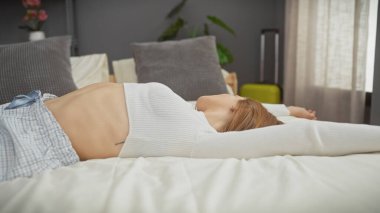 Kafkasyalı genç bir kadın modern bir yatak odasında bir yatakta dinleniyor, bir ev ortamında rahatlık tasvir ediyor..