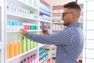 Young hispanic man customer make photo by smartphone to medicine bottle at pharmacy