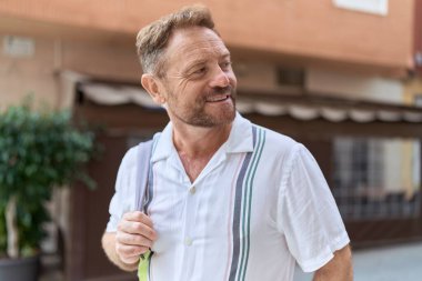 Orta yaşlı bir adam kahve dükkanının terasında kendinden emin bir şekilde gülümsüyor.