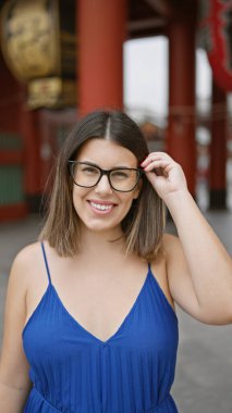 Gülümseyen ve neşeli, gözlüklü güzel İspanyol kadın Tokyo 'daki sembolik senso ji türbesine özgüvenle poz veriyor, doğal güzellik ve kaygısız mutluluk yayıyor.