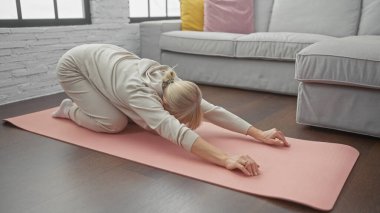 Konforlu bir oturma odasında yoga minderinin üzerinde uzanan bir kadın.