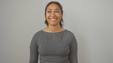 Gülümseyen genç bir İspanyol kadın. Gri bir bluzla beyaz bir arkaplanda poz veriyor.