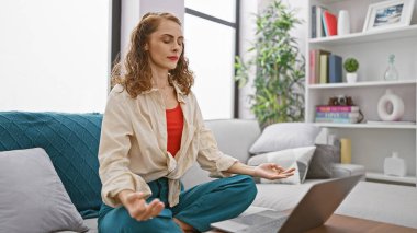 Güzel genç bir kadın dengeyi buluyor, güneşli oturma odasında huzurlu bir yoga yapıyor, evdeki rahat koltukta rahatça oturuyor.