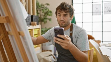 Mobil ekranına hevesle odaklanmış, kendine güvenen genç sakallı sanatçı, üniversite atölyesinin canlı sanat merkezindeki akıllı telefonuna titizlikle çiziyor.