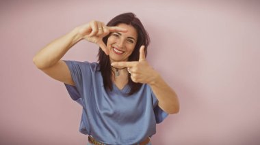 Gülümseyen orta yaşlı İspanyol bir kadın pembe izole bir arka plana karşı elleriyle bir çerçeve oluşturuyor..