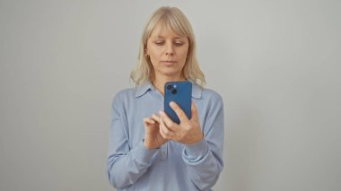 Odaklanmış beyaz bir kadın, beyaz bir arka plana karşı akıllı bir telefonla günlük kıyafet mesajları atıyor.