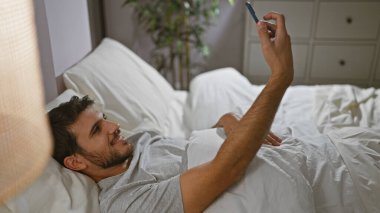 Sakallı genç bir İspanyol, rahat bir yatak odası ortamında özçekim yapıyor..