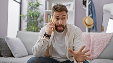 Genç İspanyol adam akıllı telefondan konuşuyor. Evdeki kanepede oturuyor.