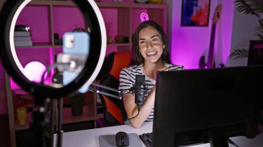 Young beautiful hispanic woman streamer smiling confident having video call at gaming room