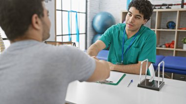 Üniformalı bir erkek terapist, fizyoterapi kliniğindeki bir erkek hastayı dikkatle dinler..