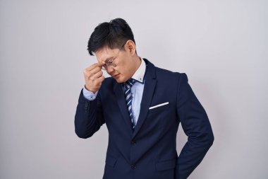 Genç Asyalı takım elbiseli ve kravatlı adam yorgun burnu ve gözleri ovuşturup yorgun ve baş ağrısı çekiyor. Stres ve hüsran kavramı. 