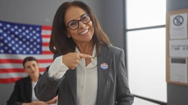 Gözlüklü, kendine güvenen bir kadın başka bir kadın ve arkasında Amerikan bayrağı olan bir odada 