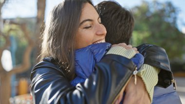 Güneşli bir parkta bir adamı kucaklayan mutlu bir kadın sevgi ve yakınlık gösteriyor..