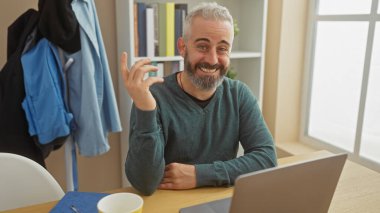 Samimi bir ofis ortamında görüntülü konuşma yaparken gülümseyen sakallı bir adam..