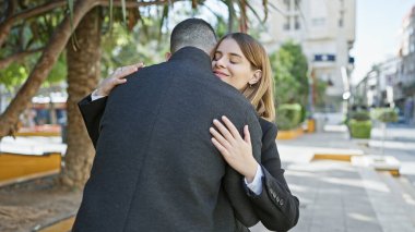 Erkek ve kadın, ağaçlar ve banklarla dolu güneşli bir caddede sevgiyle kucaklaşıyorlar..