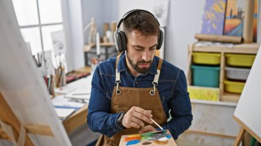 Genç İspanyol erkek sanatçı, resim stüdyosuna odaklanmış, fırça, tuval ve boya arasında müzik dinlerken bir portre çiziyor.