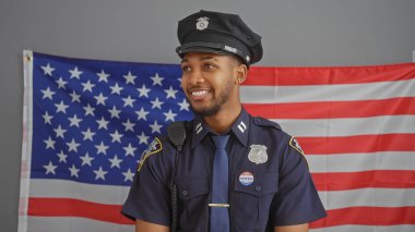 Yakışıklı Afro-Amerikan polisi Amerikan bayrağının önünde gururla gülümsüyor..