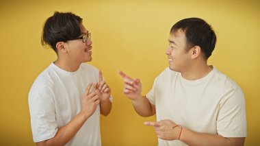 Beyaz gömlekli iki Asyalı, sarı arka plana gülüp el kol hareketi yapıyor.