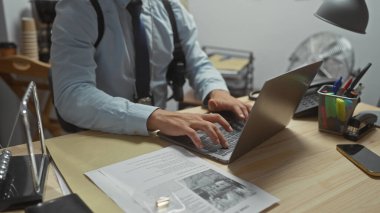 Dedektif, karakolda dizüstü bilgisayarda çalışıyor. Elinde kanıt ve ofis malzemeleri var..